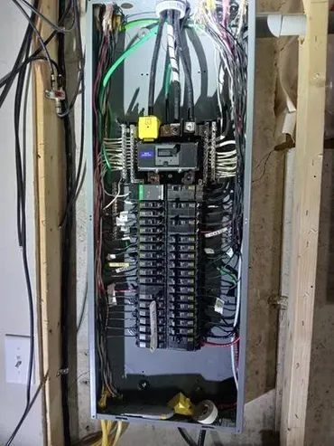 Electrical panel with numerous wires and circuit breakers, installed on a wooden frame.
