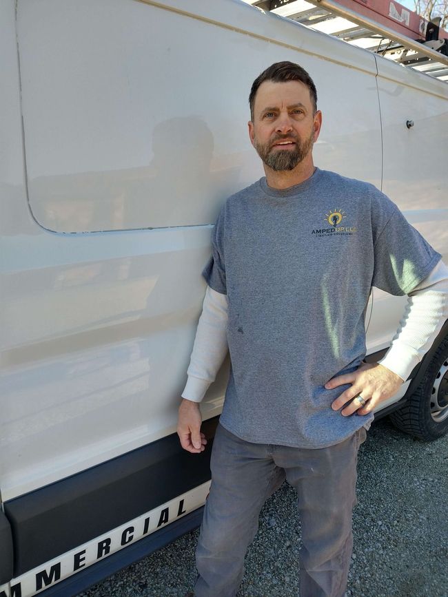 Man in gray shirt and jeans standing next to a white commercial van, smiling.