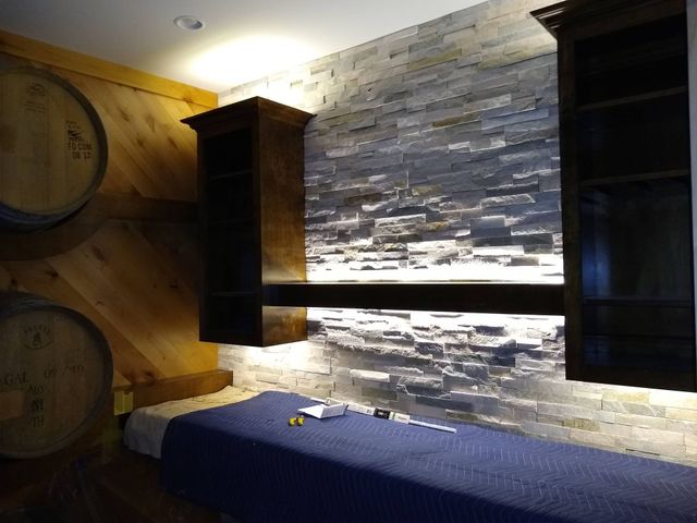 Wine cellar interior with stacked stone wall, cabinets, barrels, and a blue-covered bench.