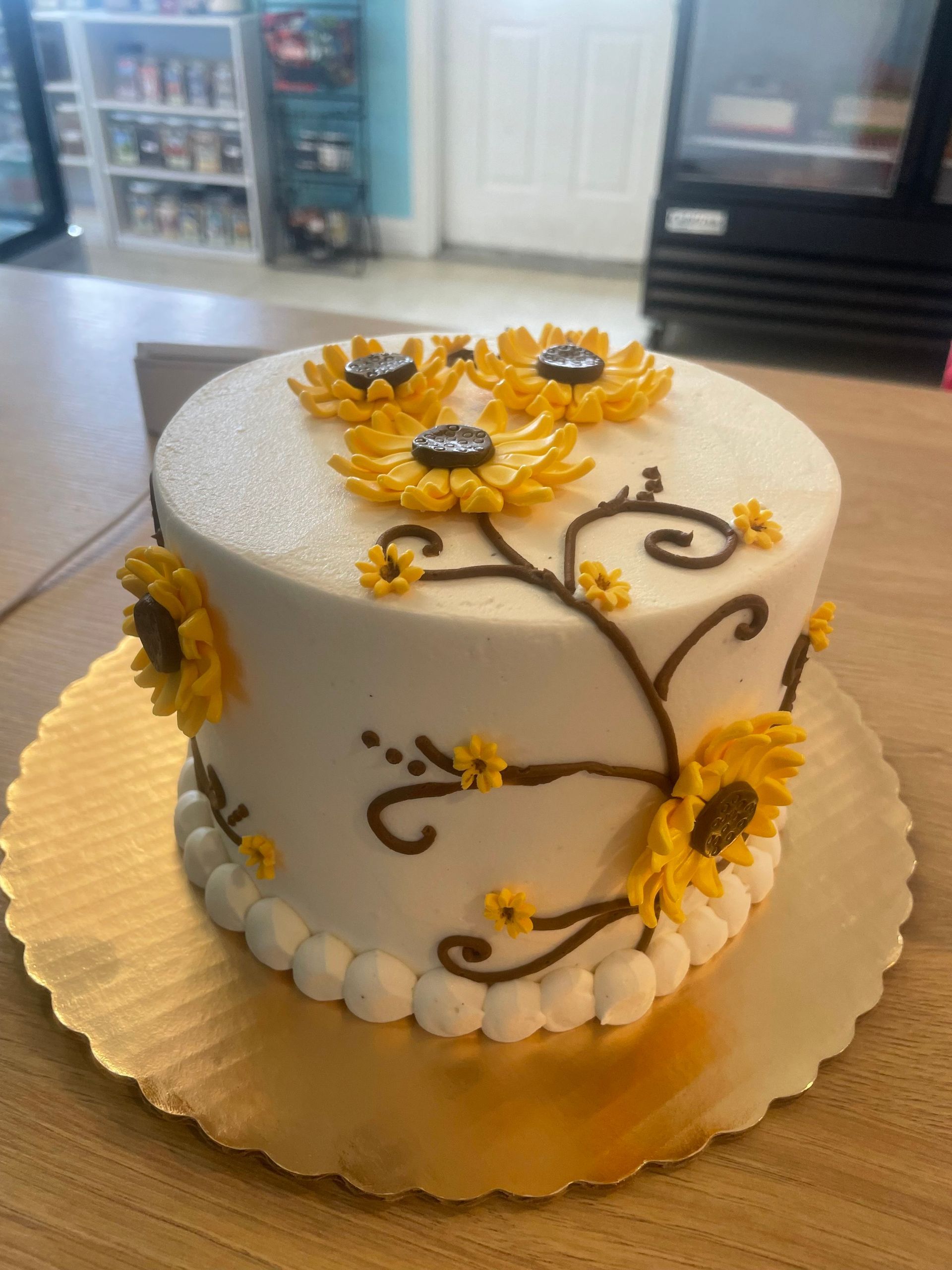A white cake with yellow sunflowers on it is sitting on a wooden table.