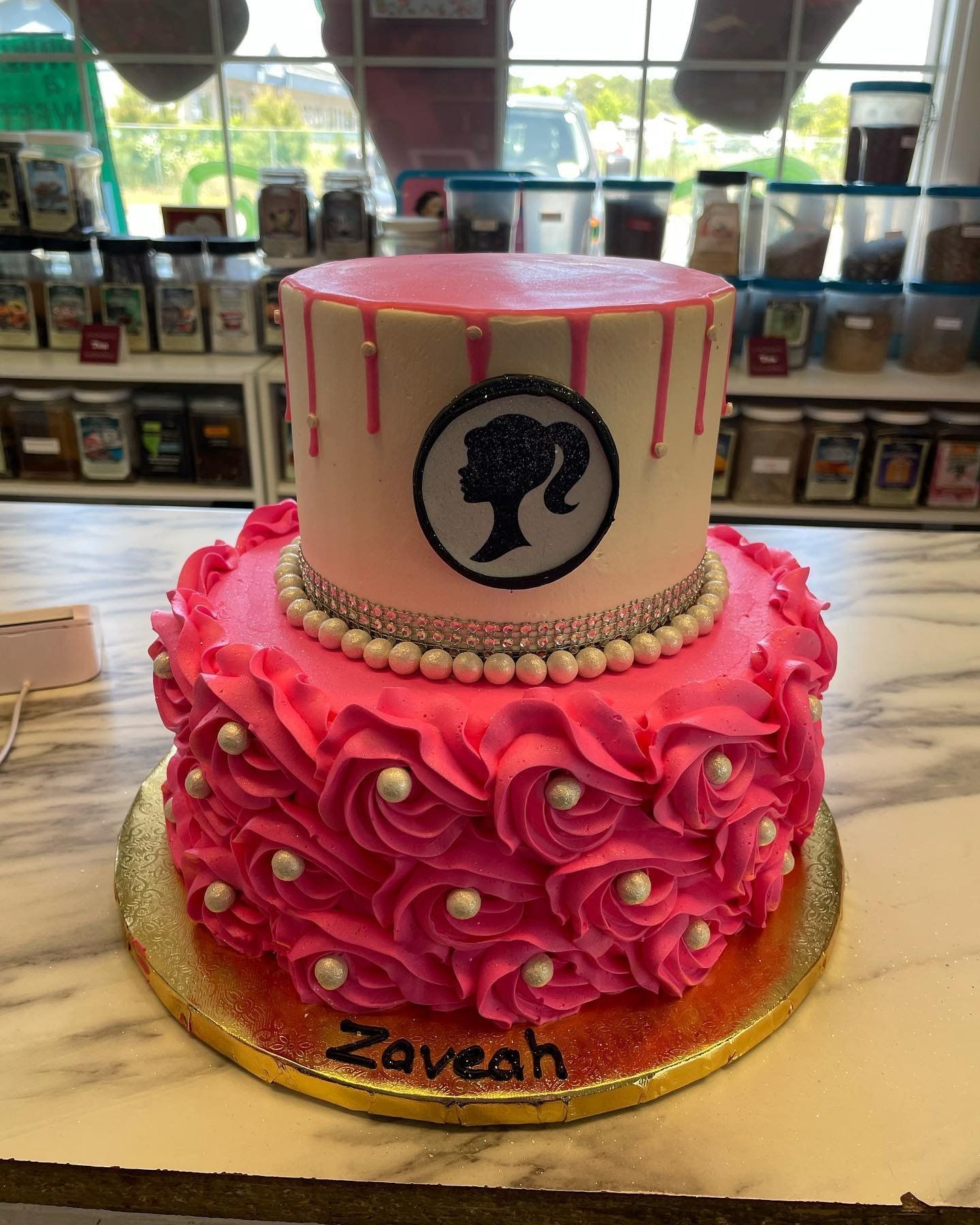 A pink and white cake with a barbie logo on it