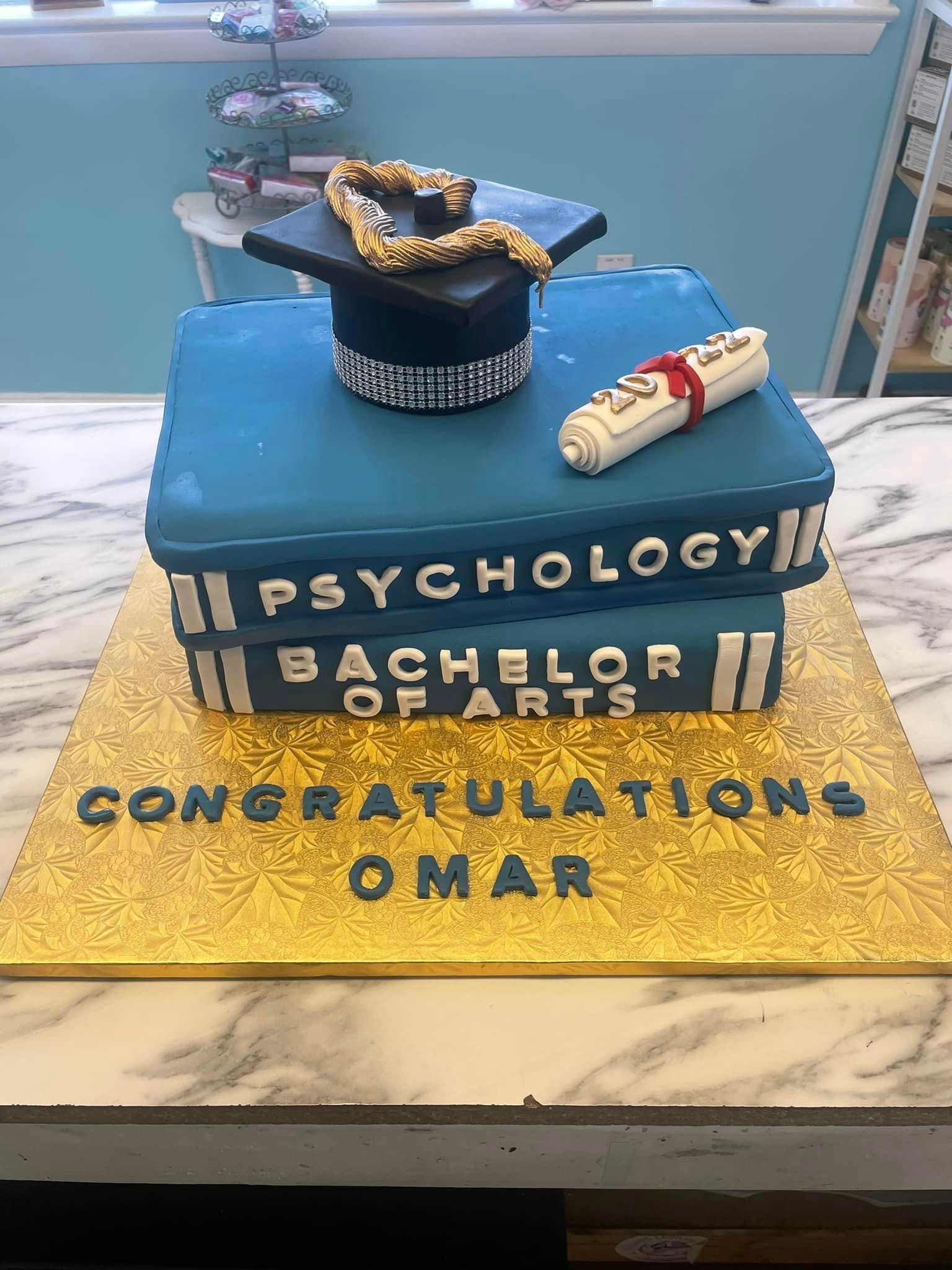 A graduation cake with a graduation cap and diploma on top of a stack of books.