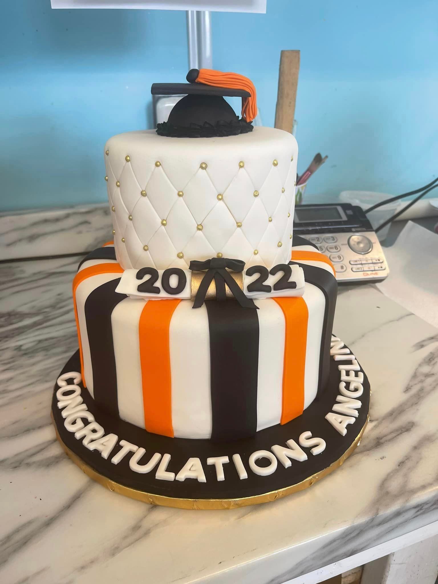 A black and orange striped cake with a graduation cap on top.