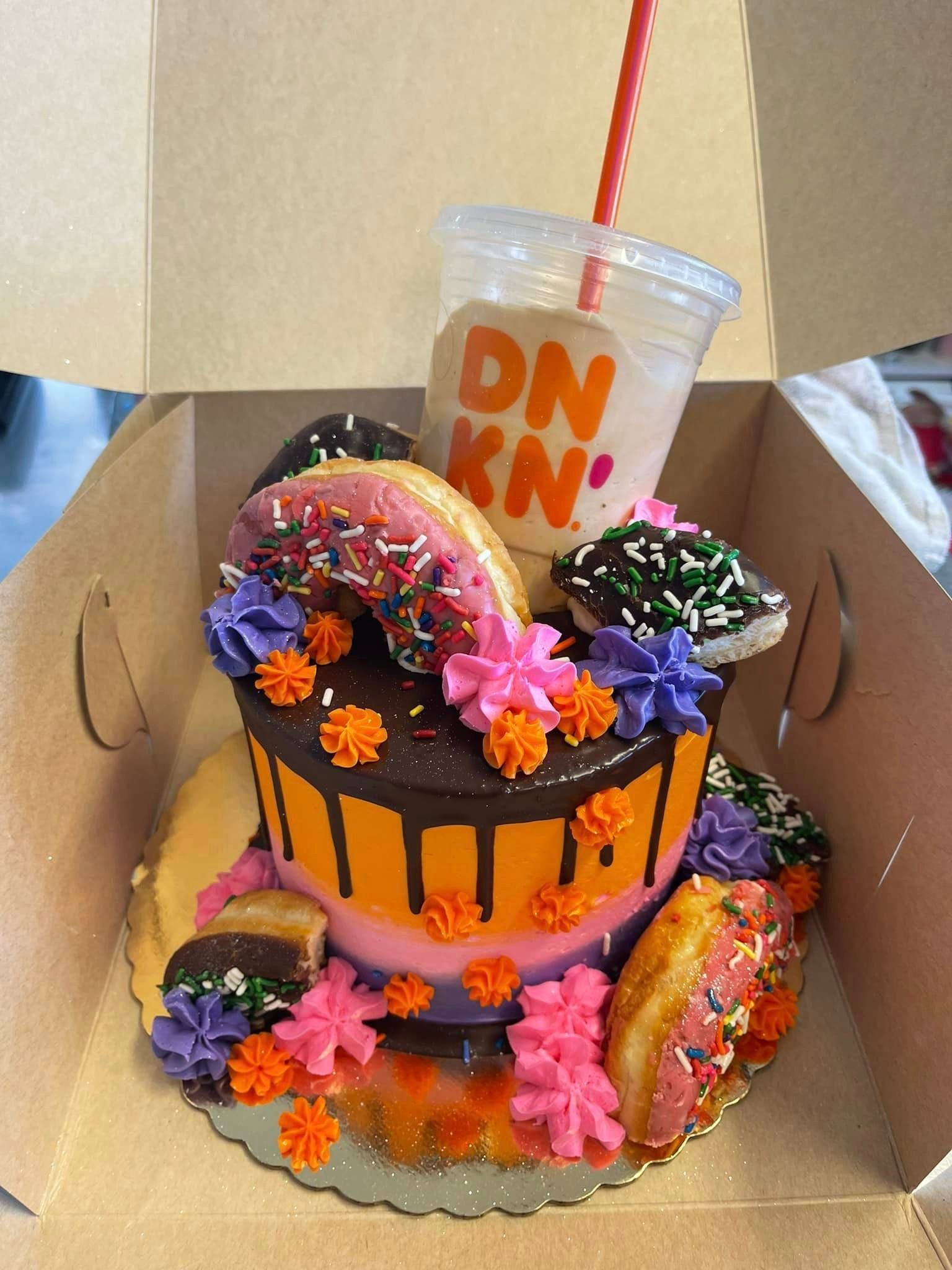 A dunkin donuts cake with donuts and flowers in a box
