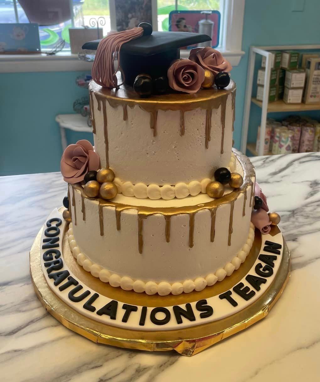 A white and gold graduation cake with a graduation cap on top.