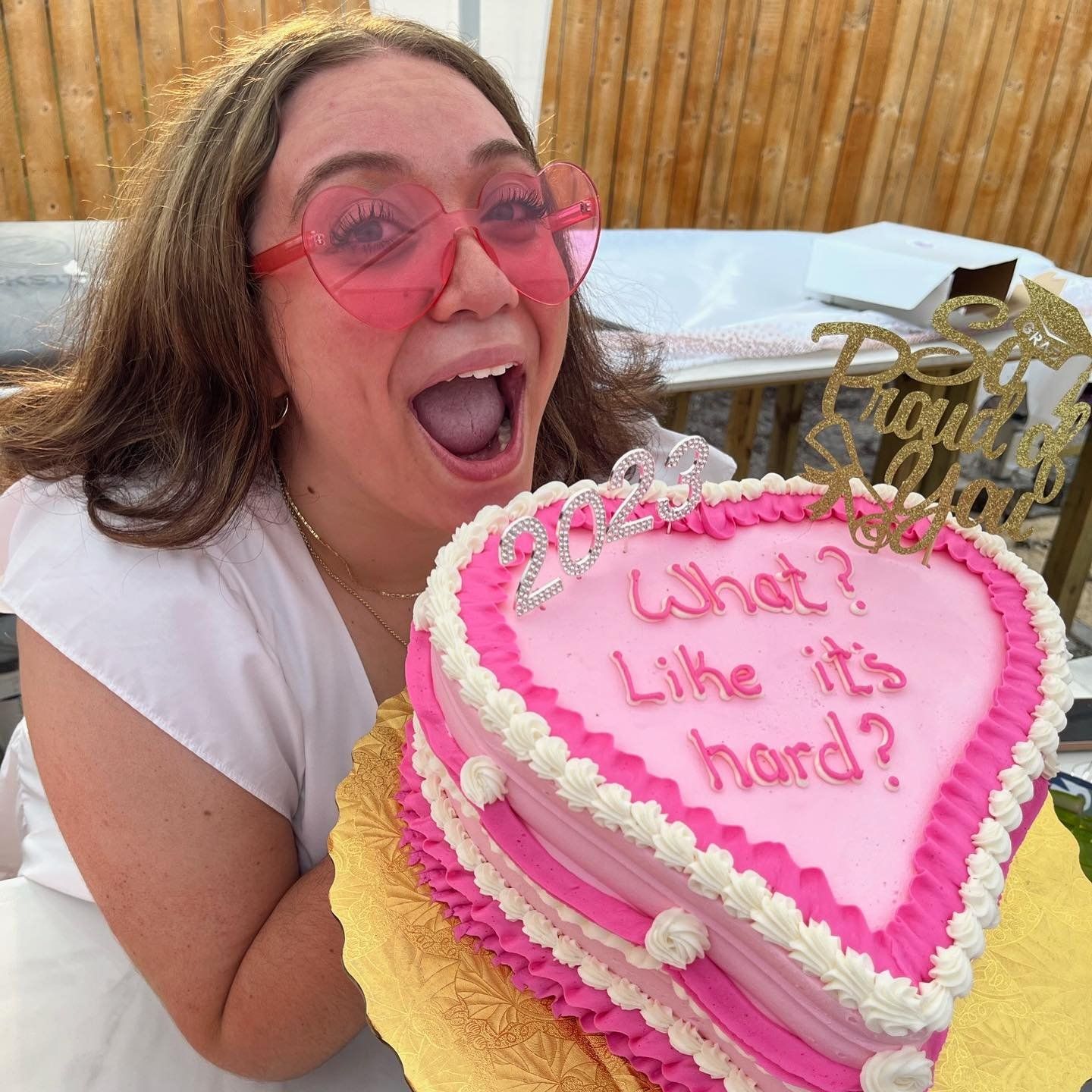 A woman is holding a pink heart shaped cake that says what ? like it 's hard ?