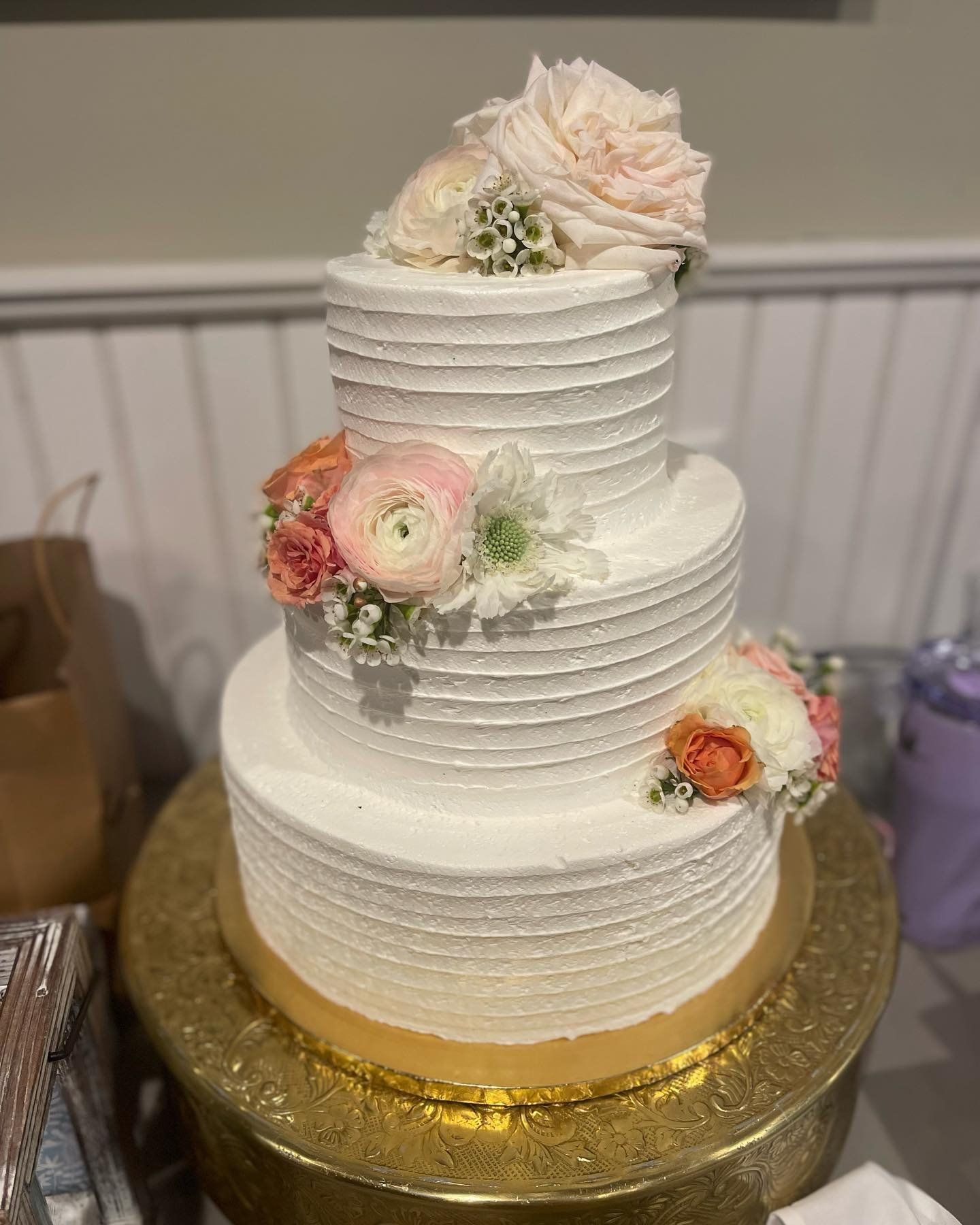 A white wedding cake with flowers on top is sitting on top of a gold cake stand.