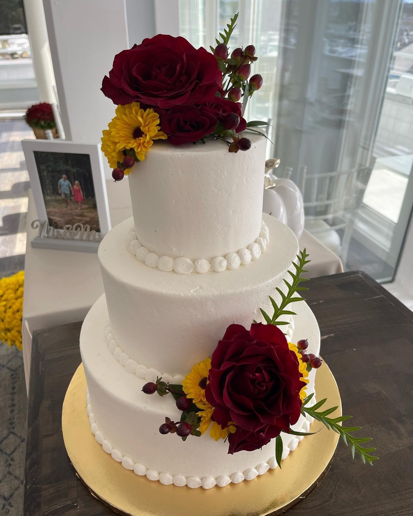 A white wedding cake with red roses and yellow flowers on it