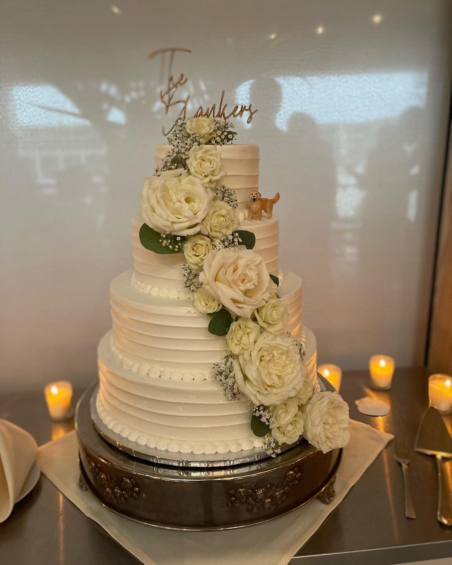 A wedding cake with white roses and a dog on top