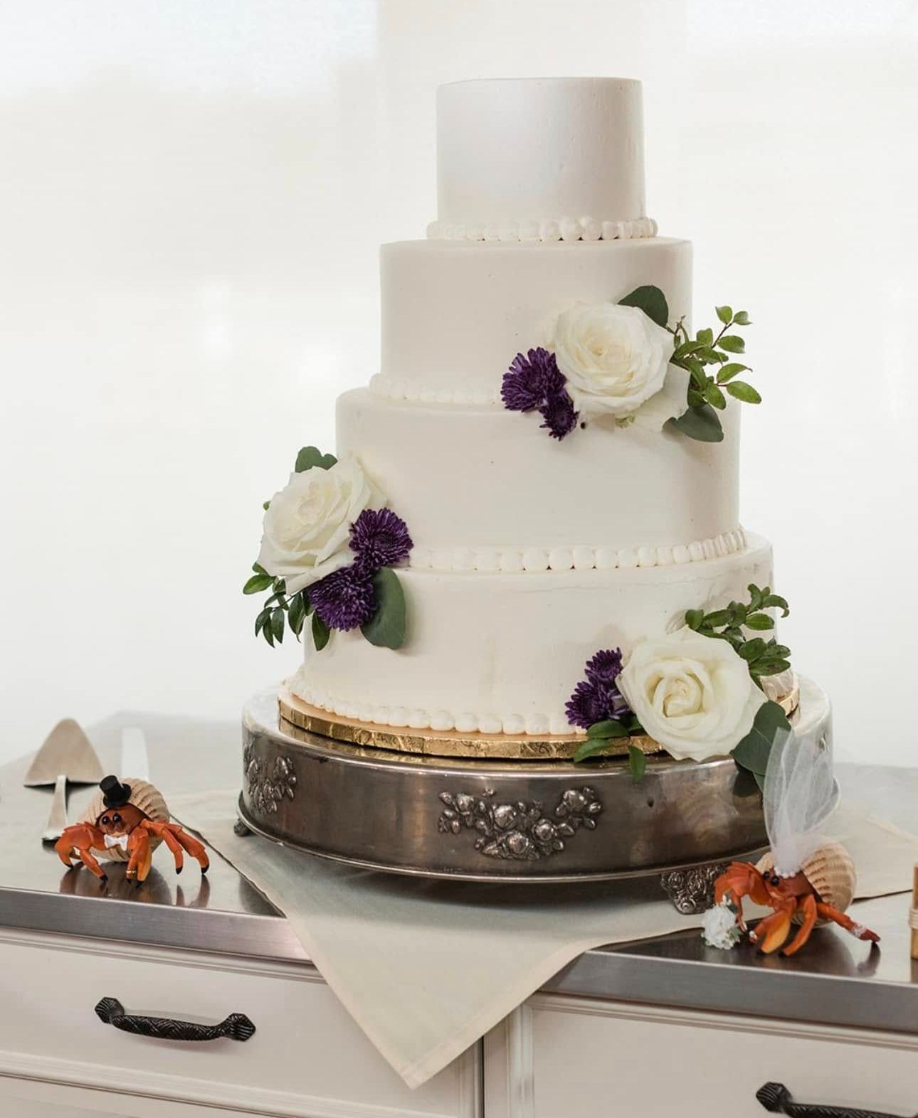 A white wedding cake with purple flowers is sitting on a table.