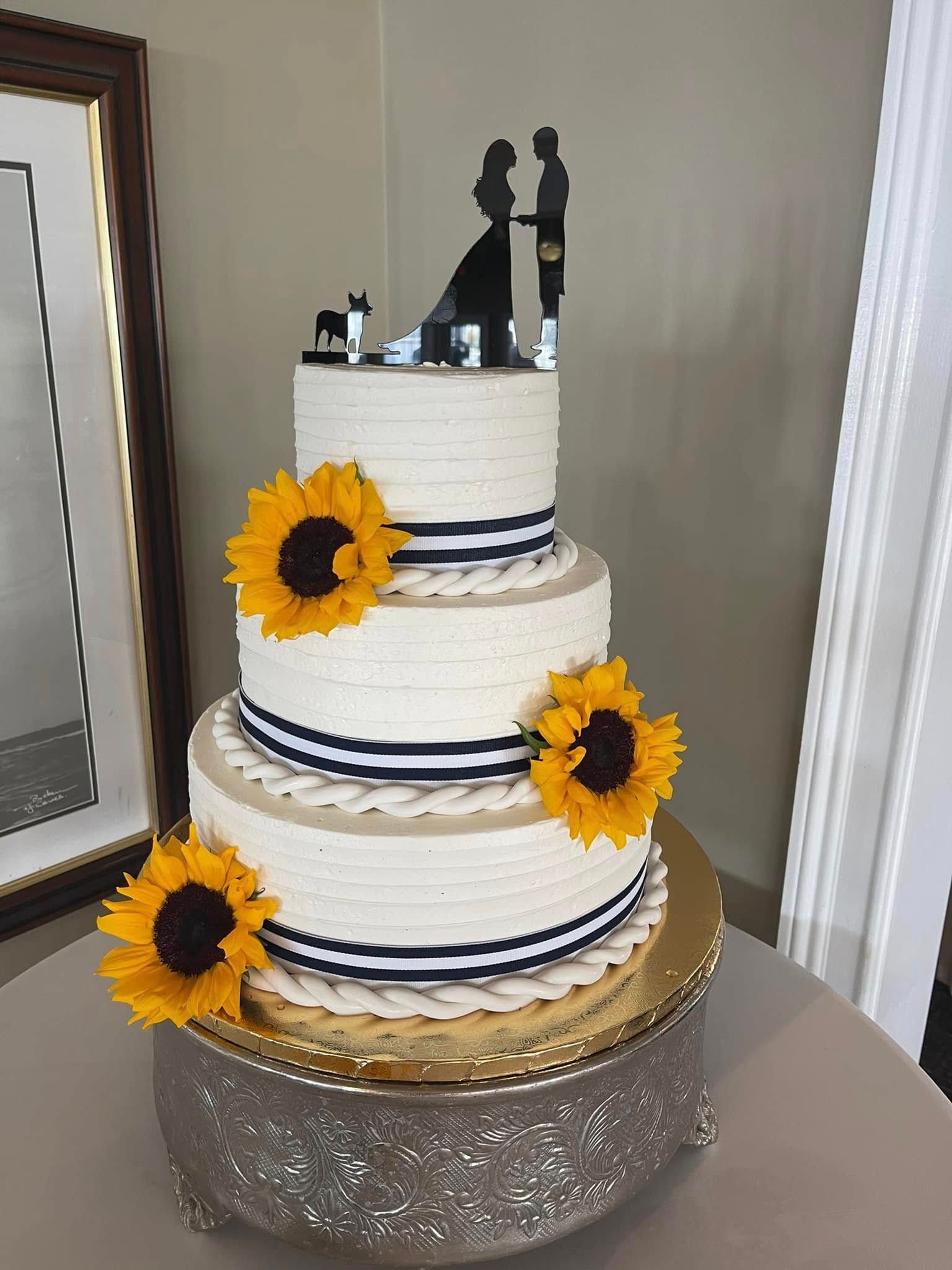 A wedding cake with sunflowers and a bride and groom topper on top of it.