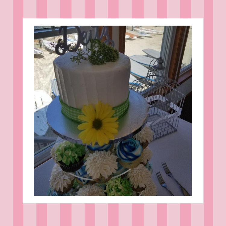 A white cake with a yellow flower on top is surrounded by cupcakes