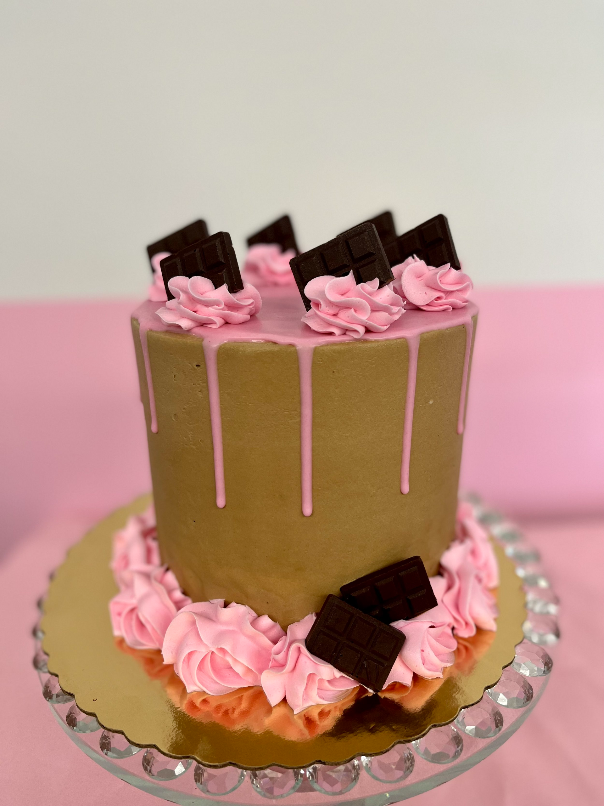 A brown cake with pink frosting and chocolate pieces on top