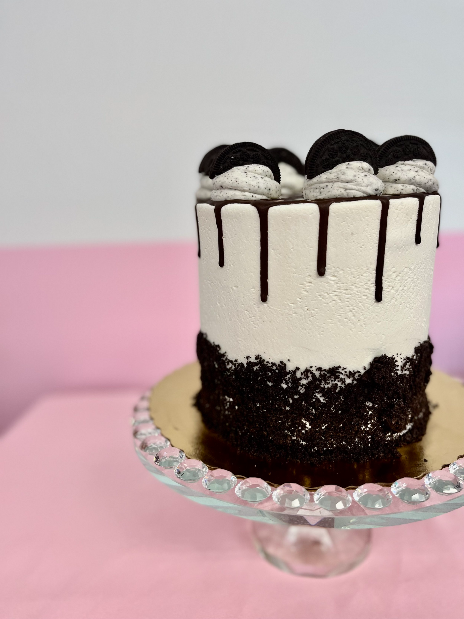 A black and white cake is sitting on a glass cake stand on a pink table.