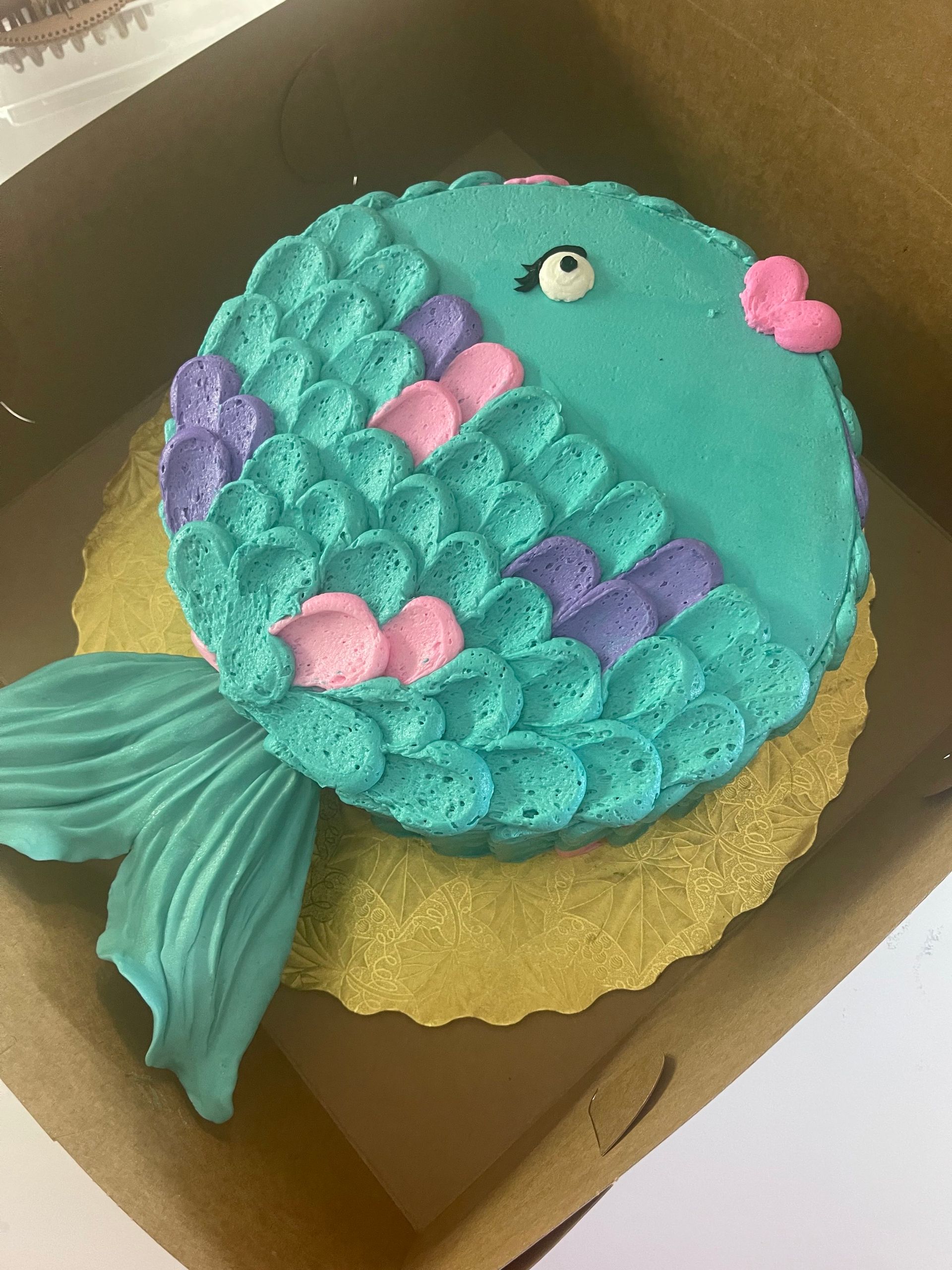 A cake decorated to look like a fish is in a box.