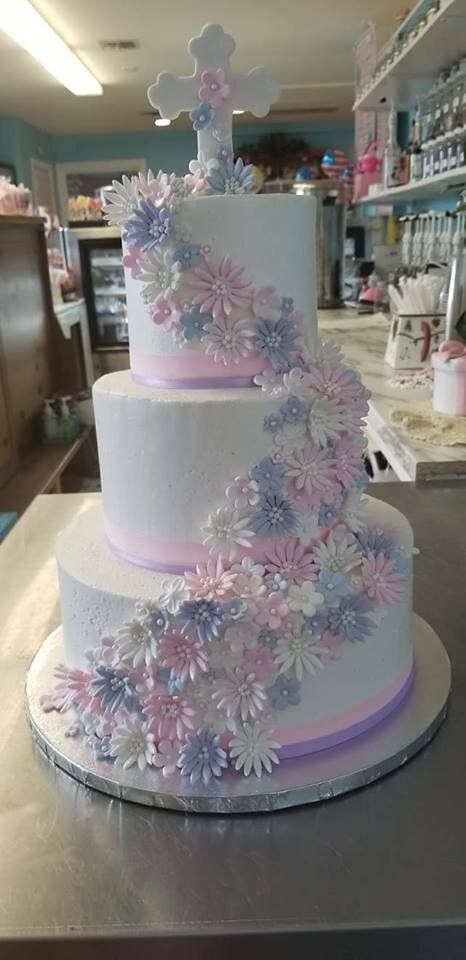 A white cake with pink and purple flowers and a cross on top is on a table.