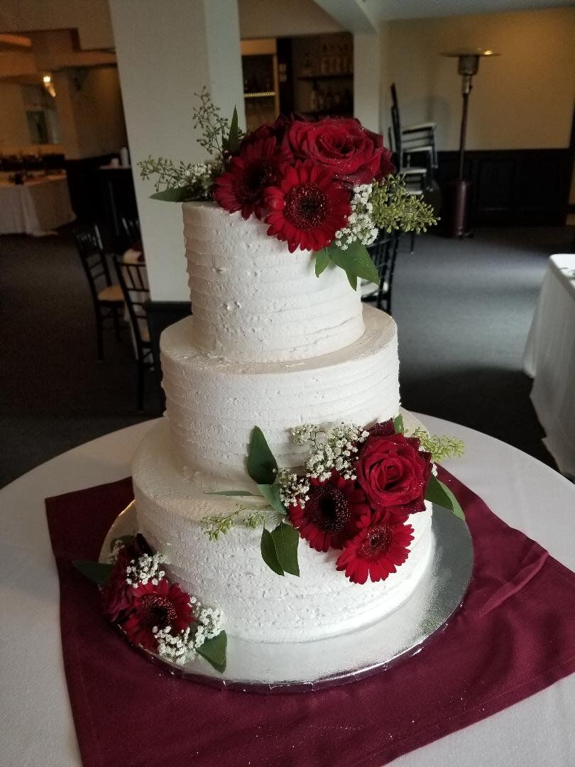 A wedding cake with red roses on top of it