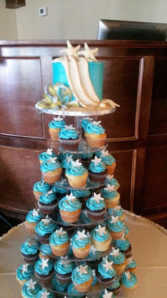 A tower of cupcakes with blue frosting and starfish on a table.