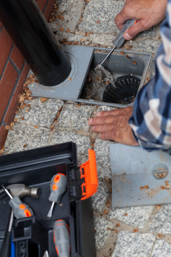 A man is fixing a drain on the sidewalk next to a toolbox.