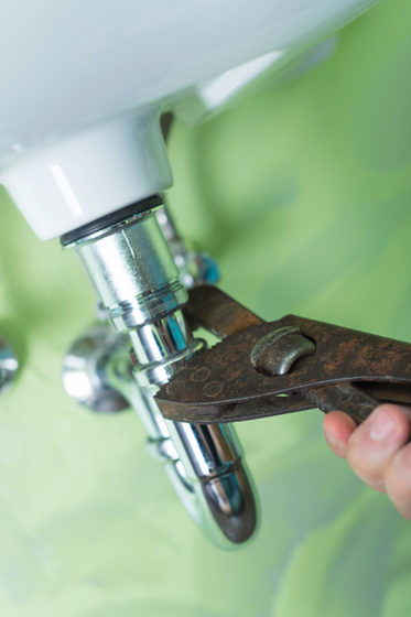 A person is fixing a sink pipe with a pair of pliers.