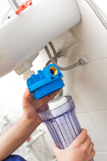 A person is installing a water filter under a sink.