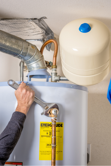 A man is fixing a water heater with a wrench.