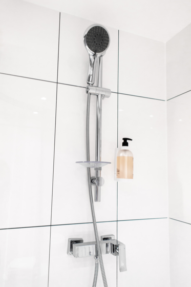 A shower head is hanging from the ceiling in a bathroom next to a soap dispenser.