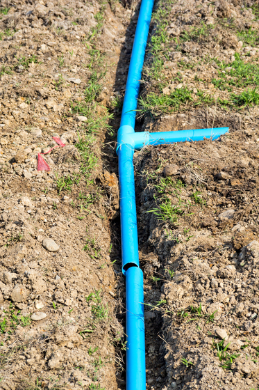 A blue pipe is laying in the dirt in a field.