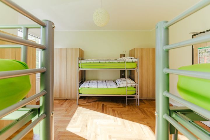 Ein Etagenbett mit grüner Bettwäsche steht in einem Zimmer mit weiteren Etagenbetten.