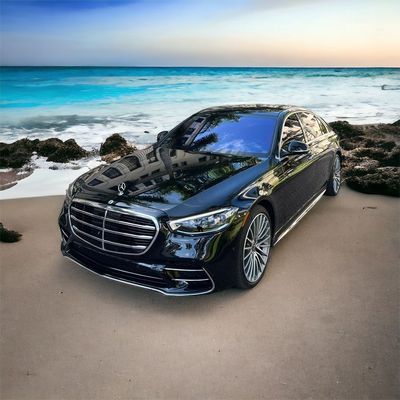 A black mercedes benz is parked on the beach near the ocean.