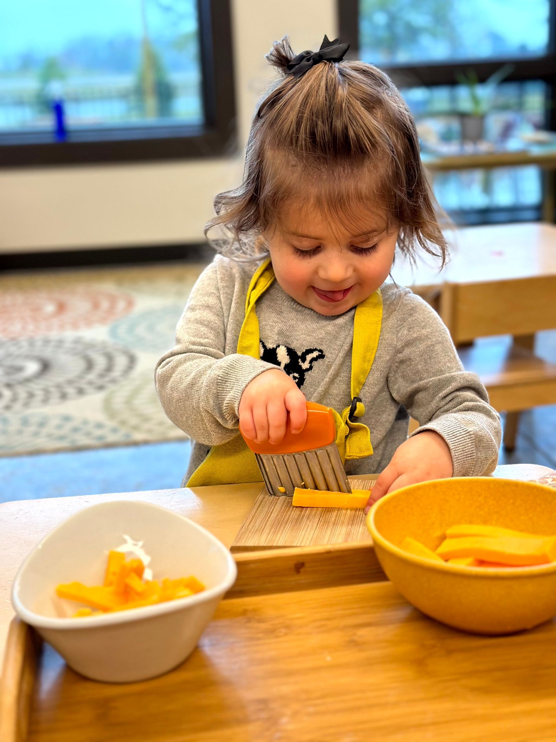 An IMA toddler student chops cheese for snack.