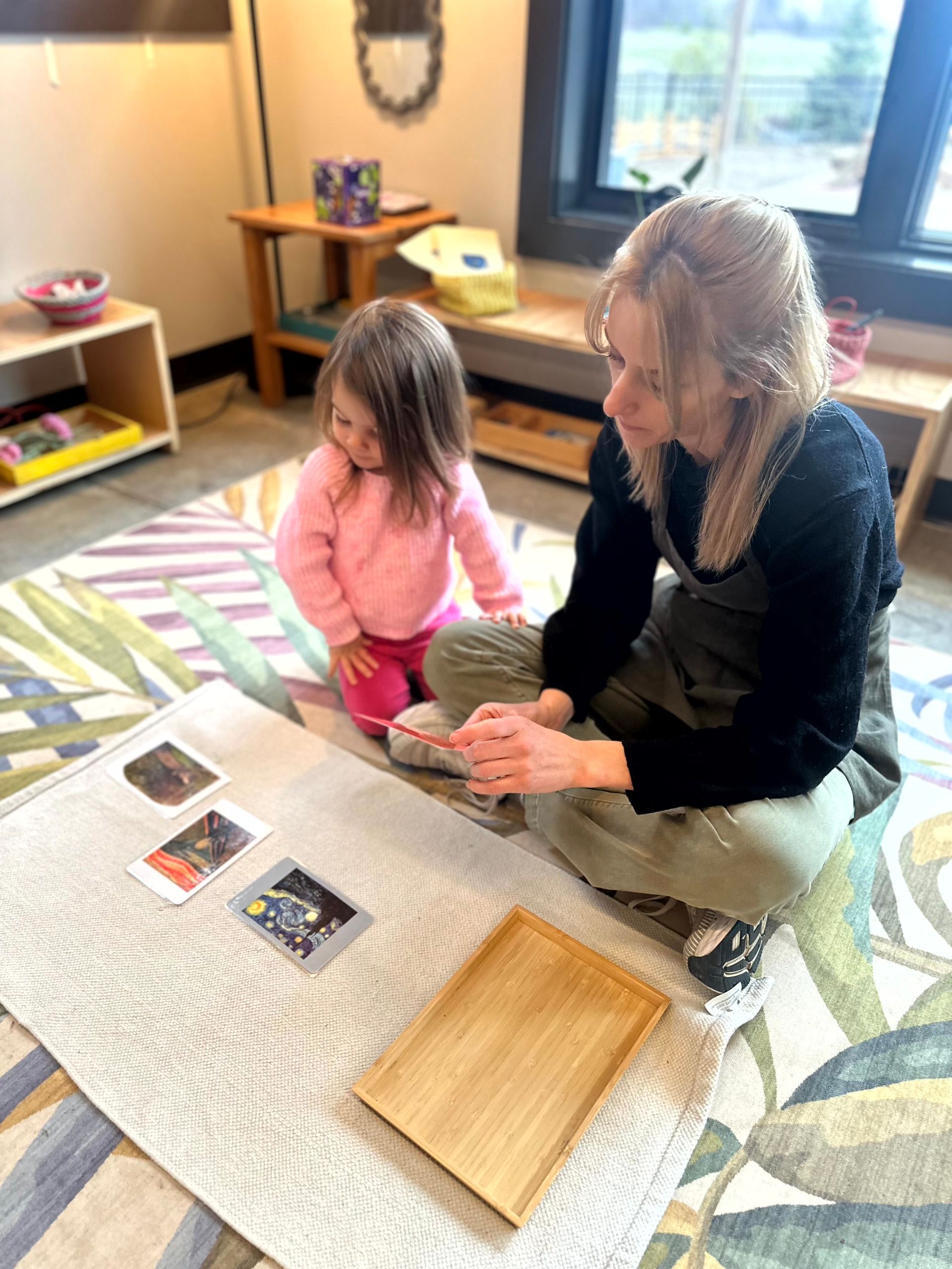 A Toddler Community assistant works with a child on nomenclature cards. 