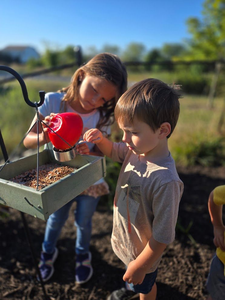 IMA children fill a bird feeder together.