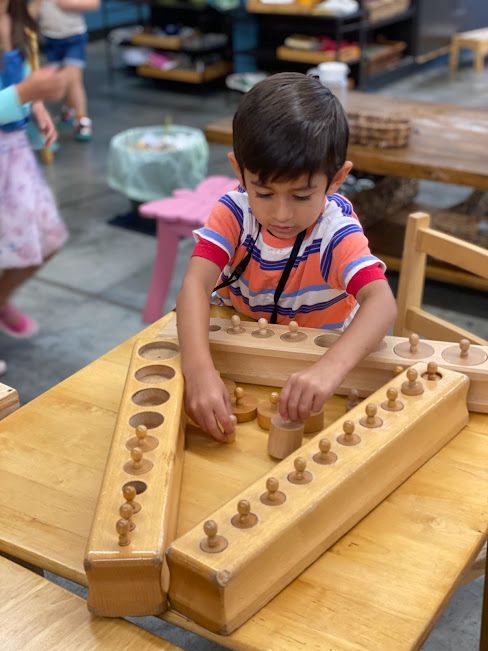 A Montessori child works with three Cylinder Blocks