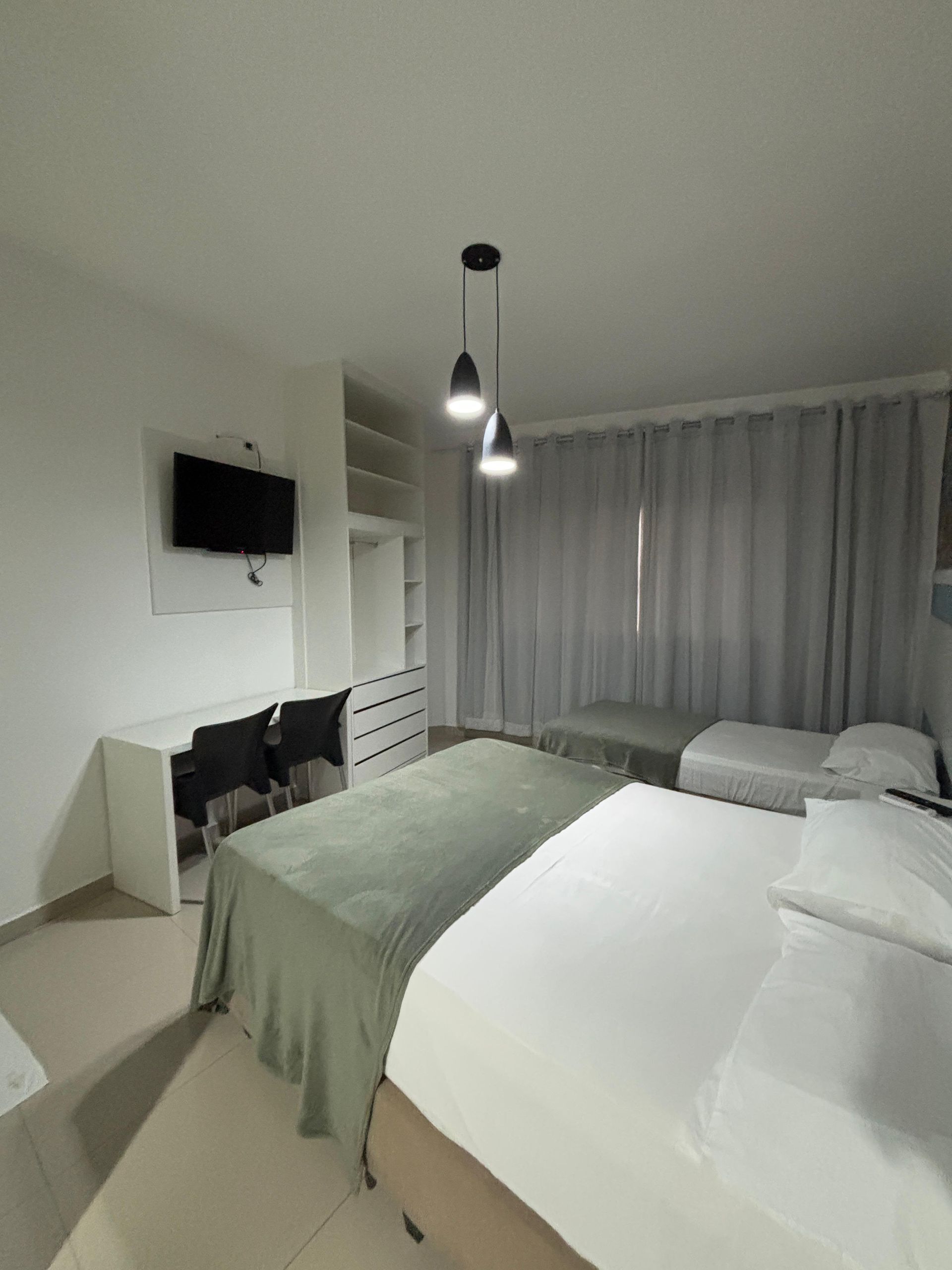 Um quarto de hotel com várias camas, uma escrivaninha com cadeiras e uma TV.