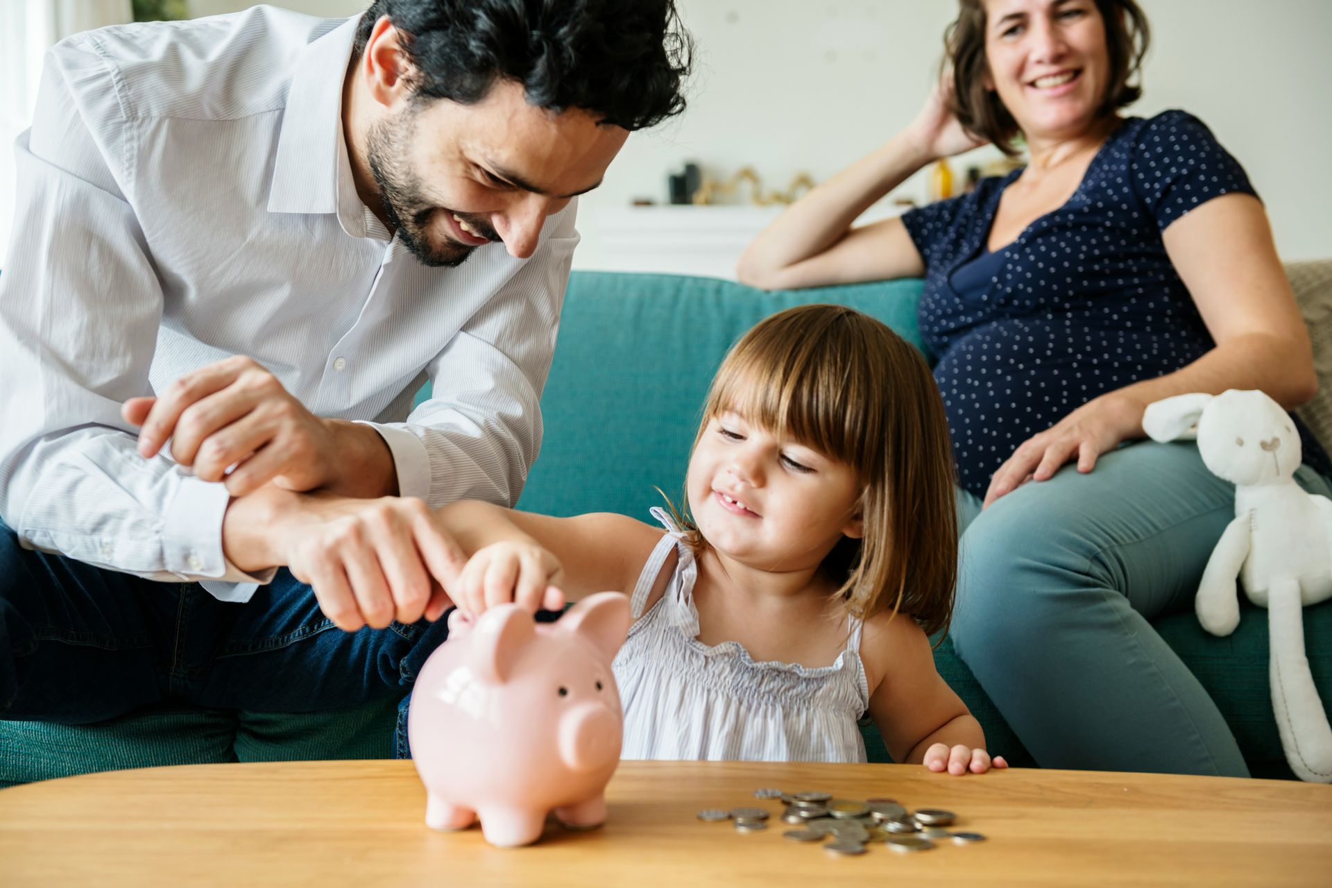 A little girl is putting coins into a piggy bank.