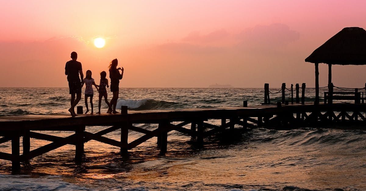 A family is standing on a pier overlooking the ocean at sunset.