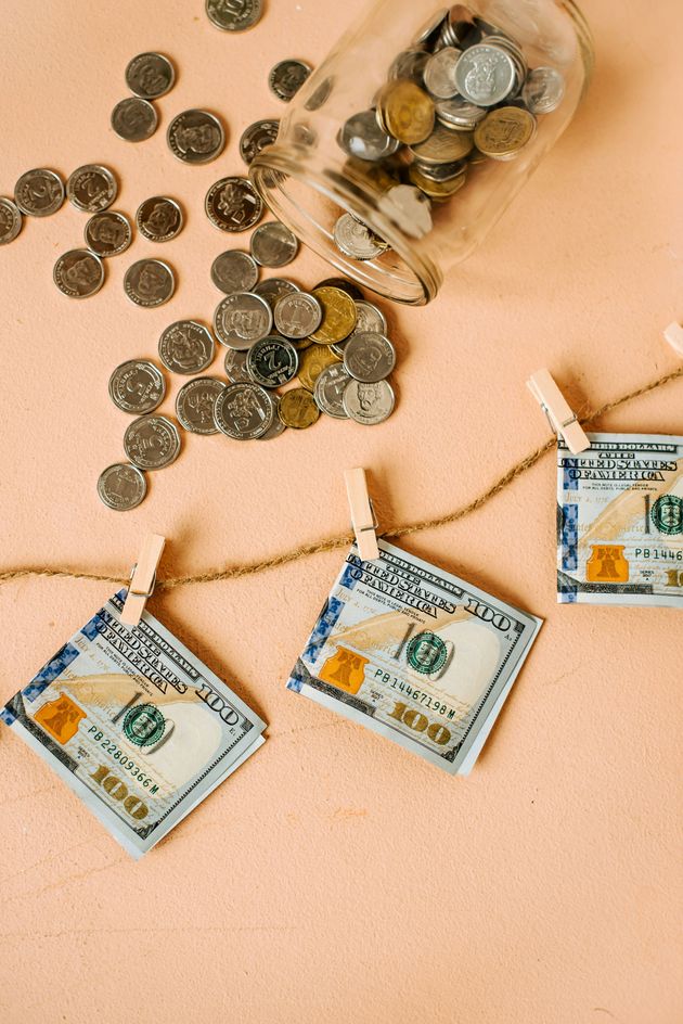 A string of money hanging on a clothesline next to a jar of coins.