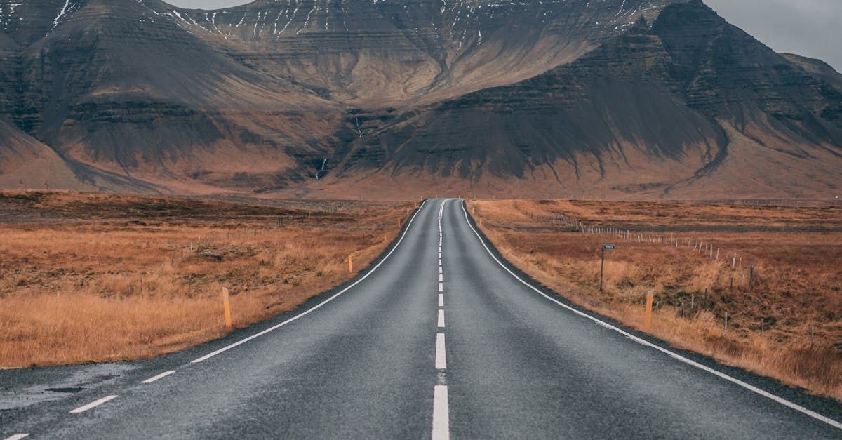 An empty road going through a desert with mountains in the background.