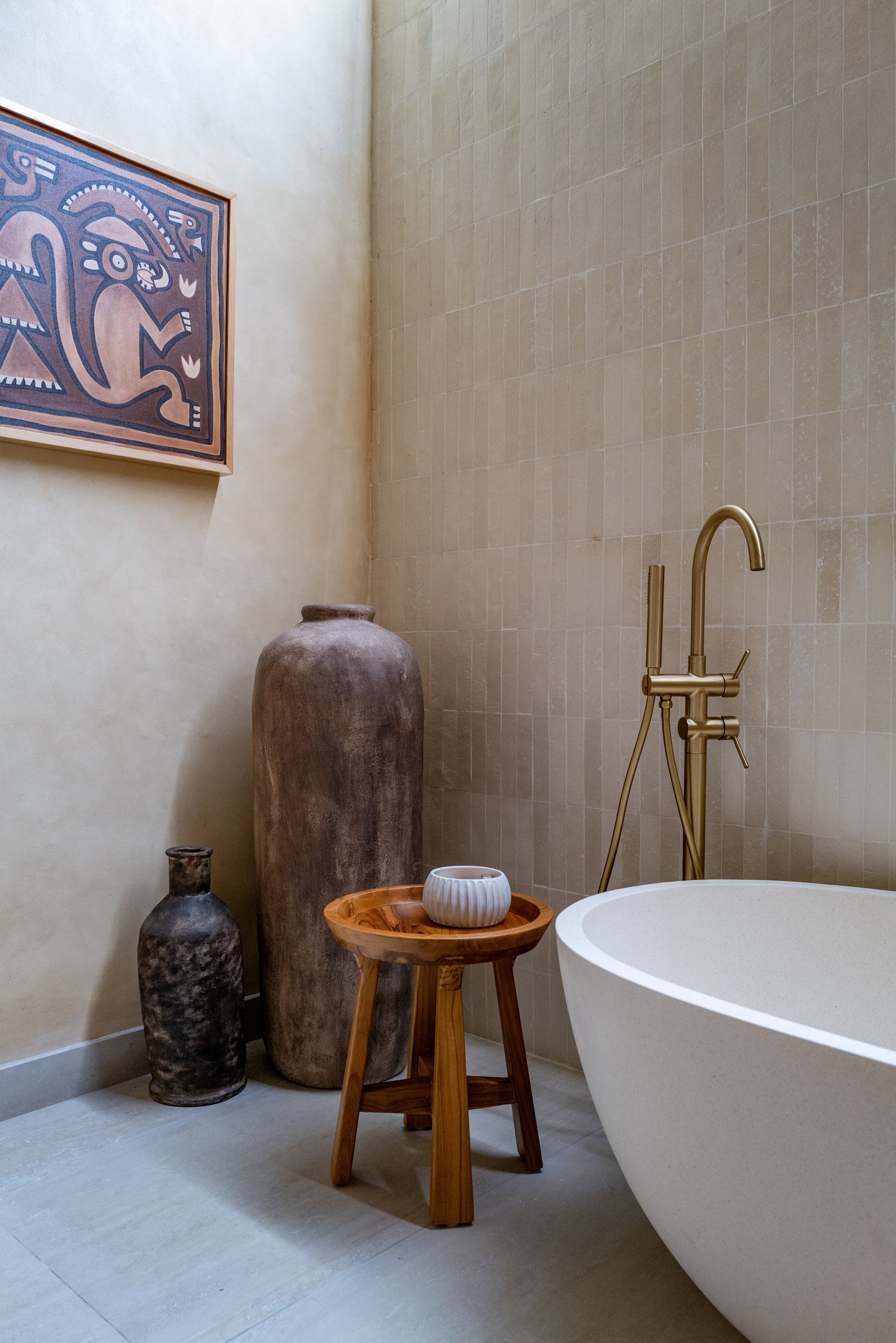 Bathroom with a freestanding bathtub, gold faucet, wooden stool, and decorative pottery.
