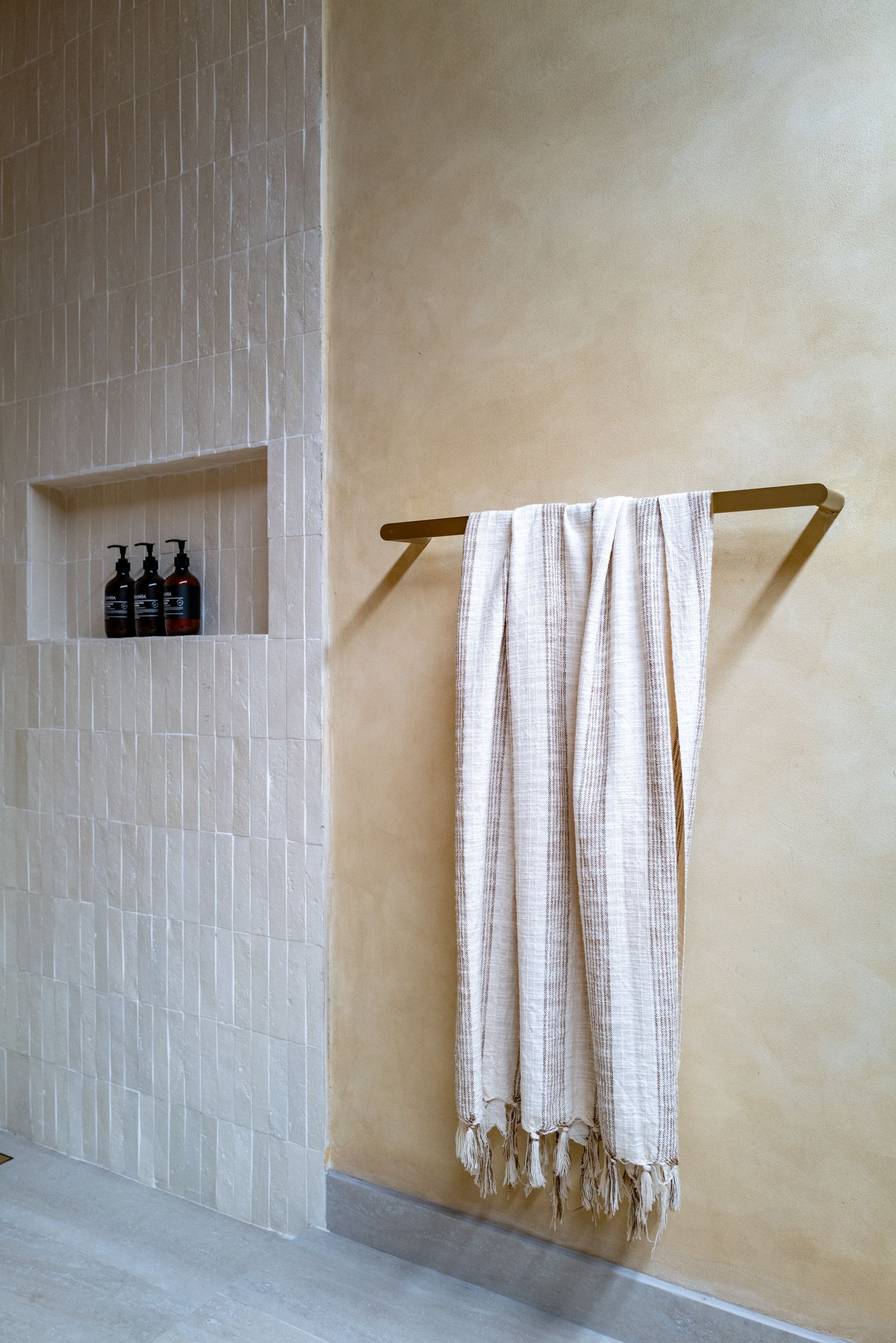 Shower with built-in shelf holding toiletries, towel bar with white throw, tan walls.