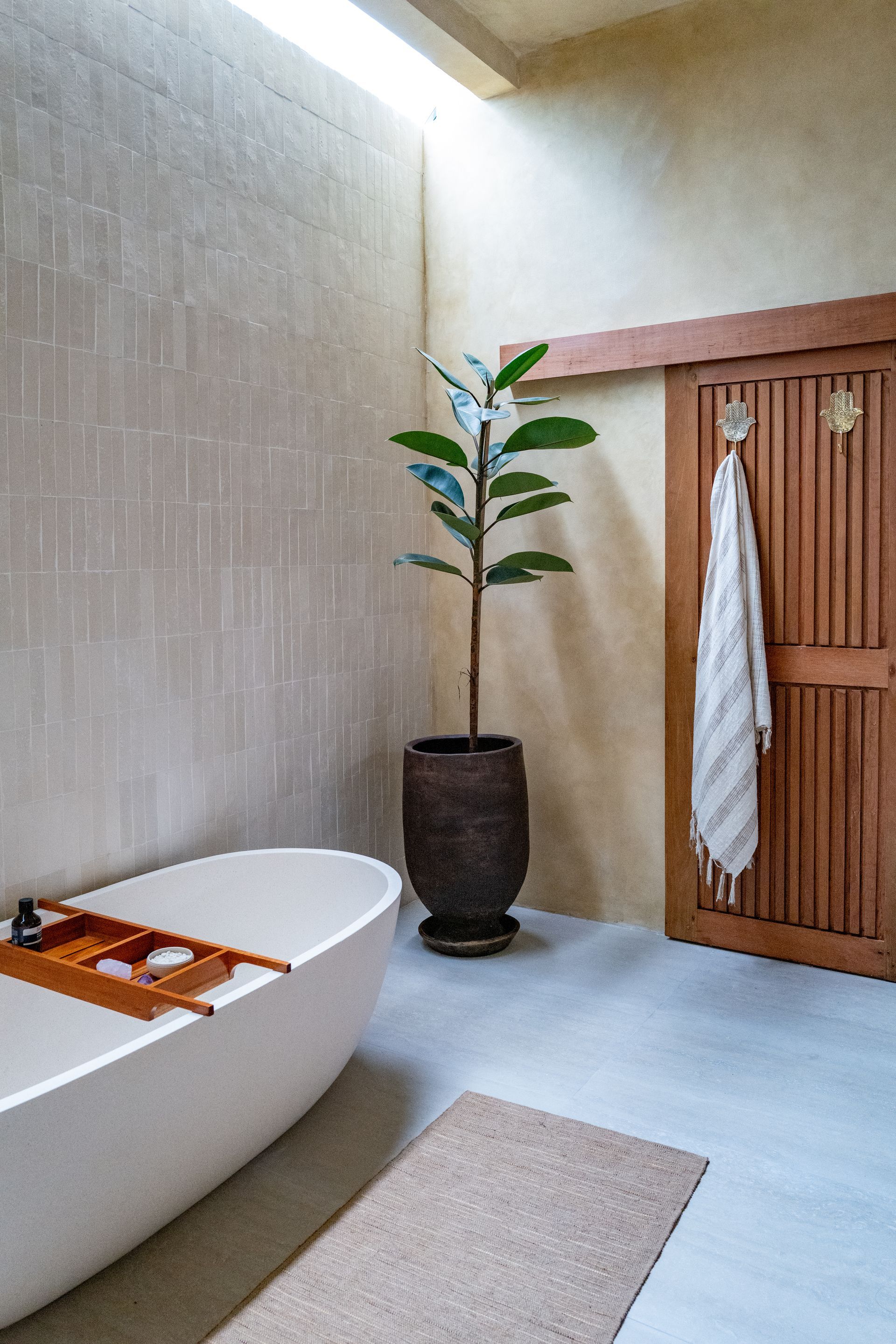 Spa-like bathroom with a white tub, plant, wooden door, and light stone walls.