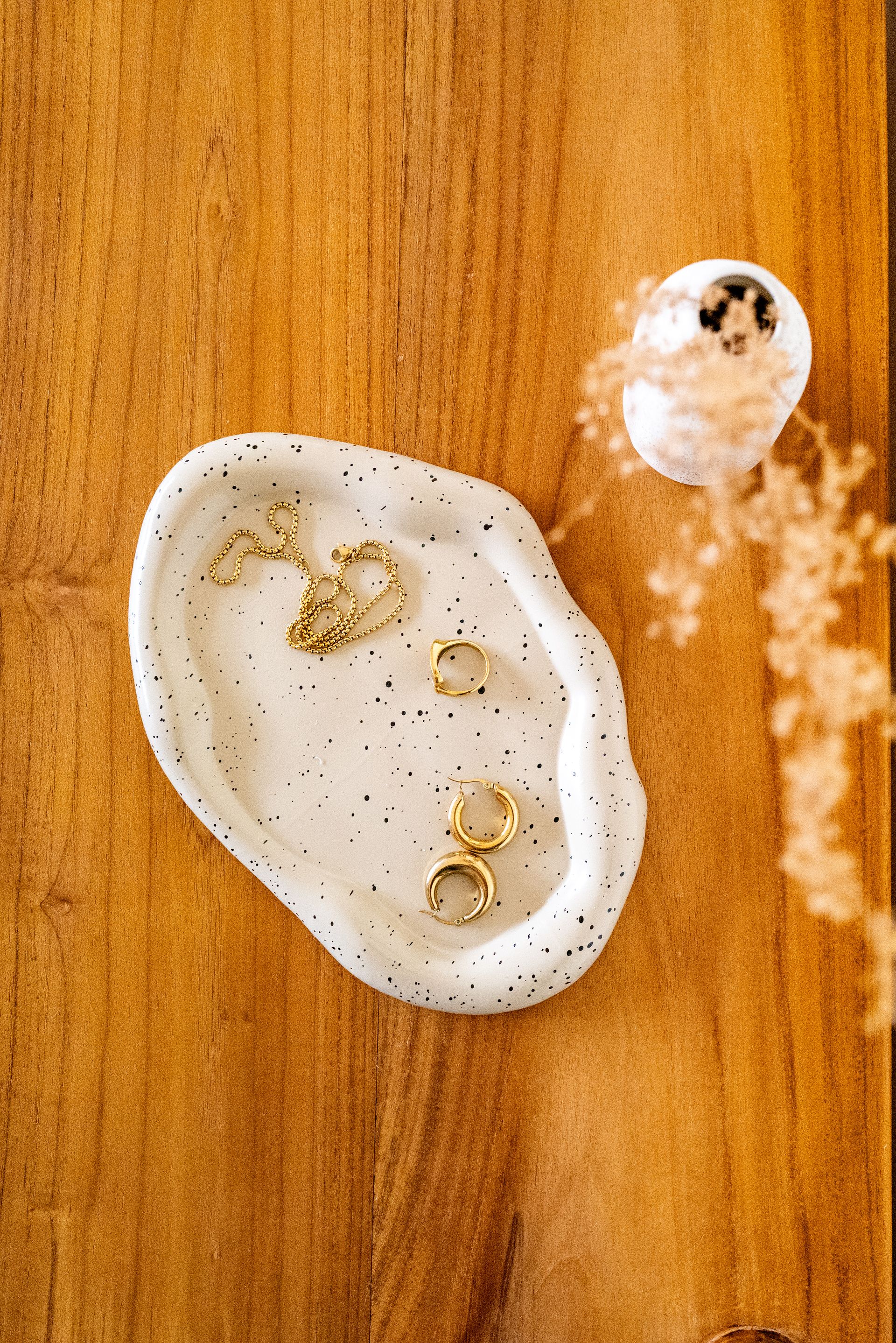 Jewelry on a speckled white ceramic tray on a wooden surface, with a small decorative object nearby.
