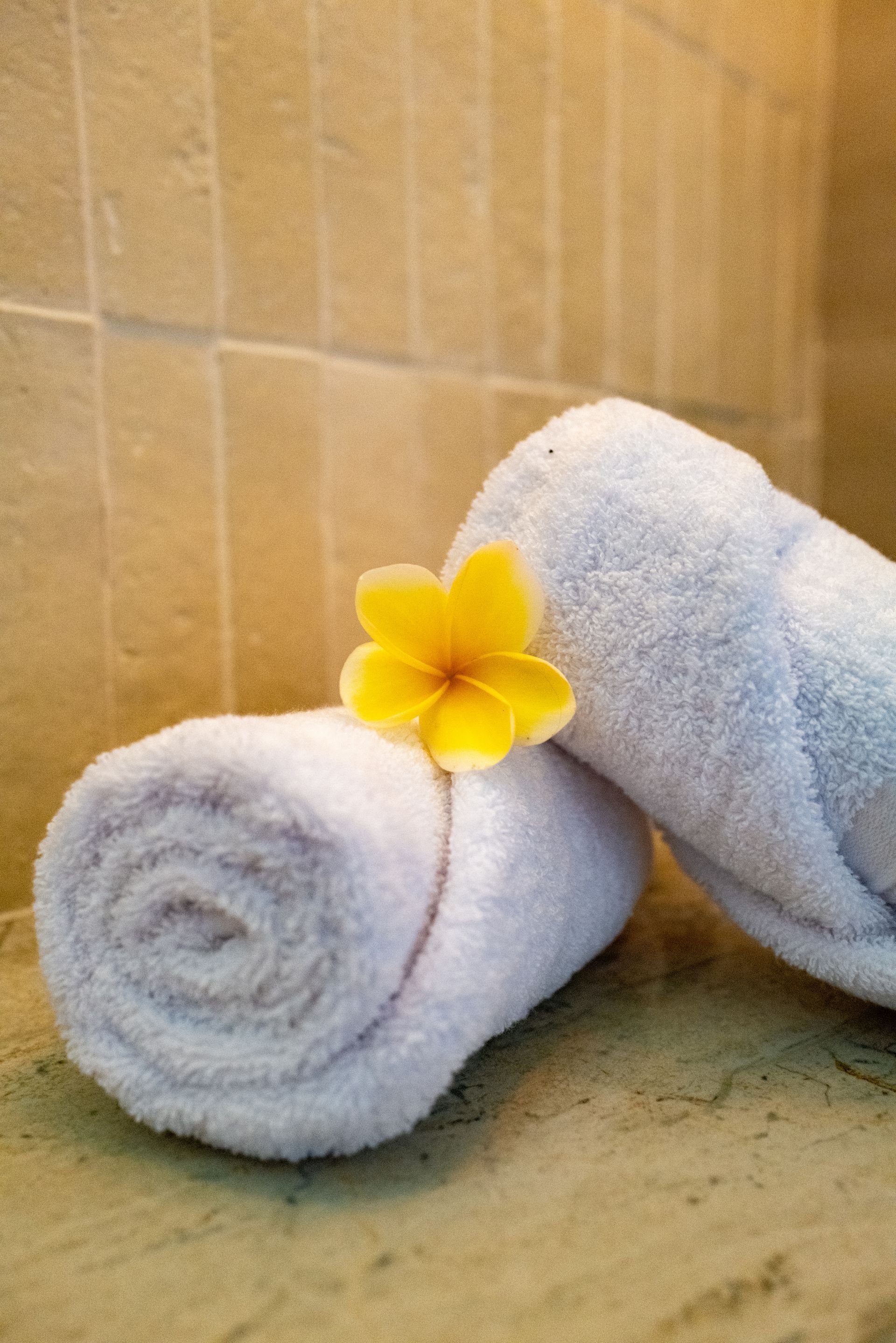 Rolled white towels with a yellow flower on a tiled surface.
