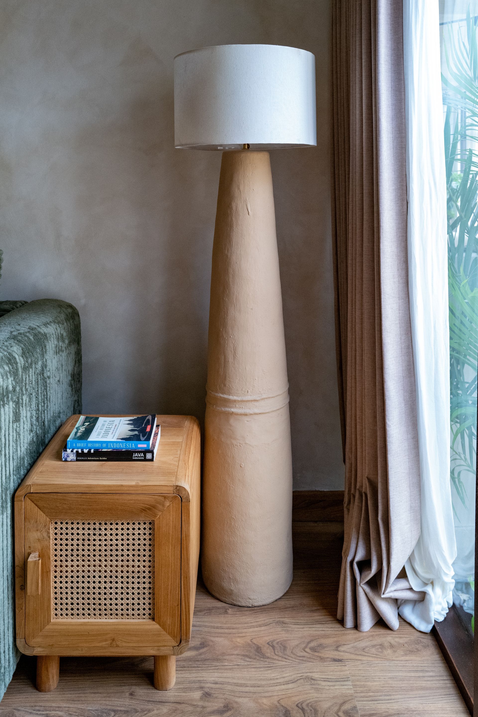 A floor lamp with a linen shade stands near a wooden side table with books. The room has a neutral color palette.