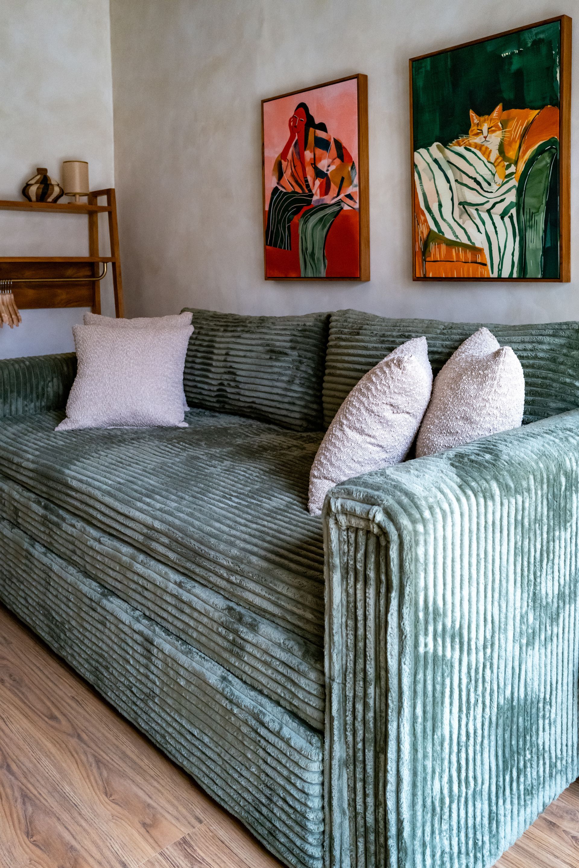 Green corduroy sofa with pillows, art, and wooden floor.