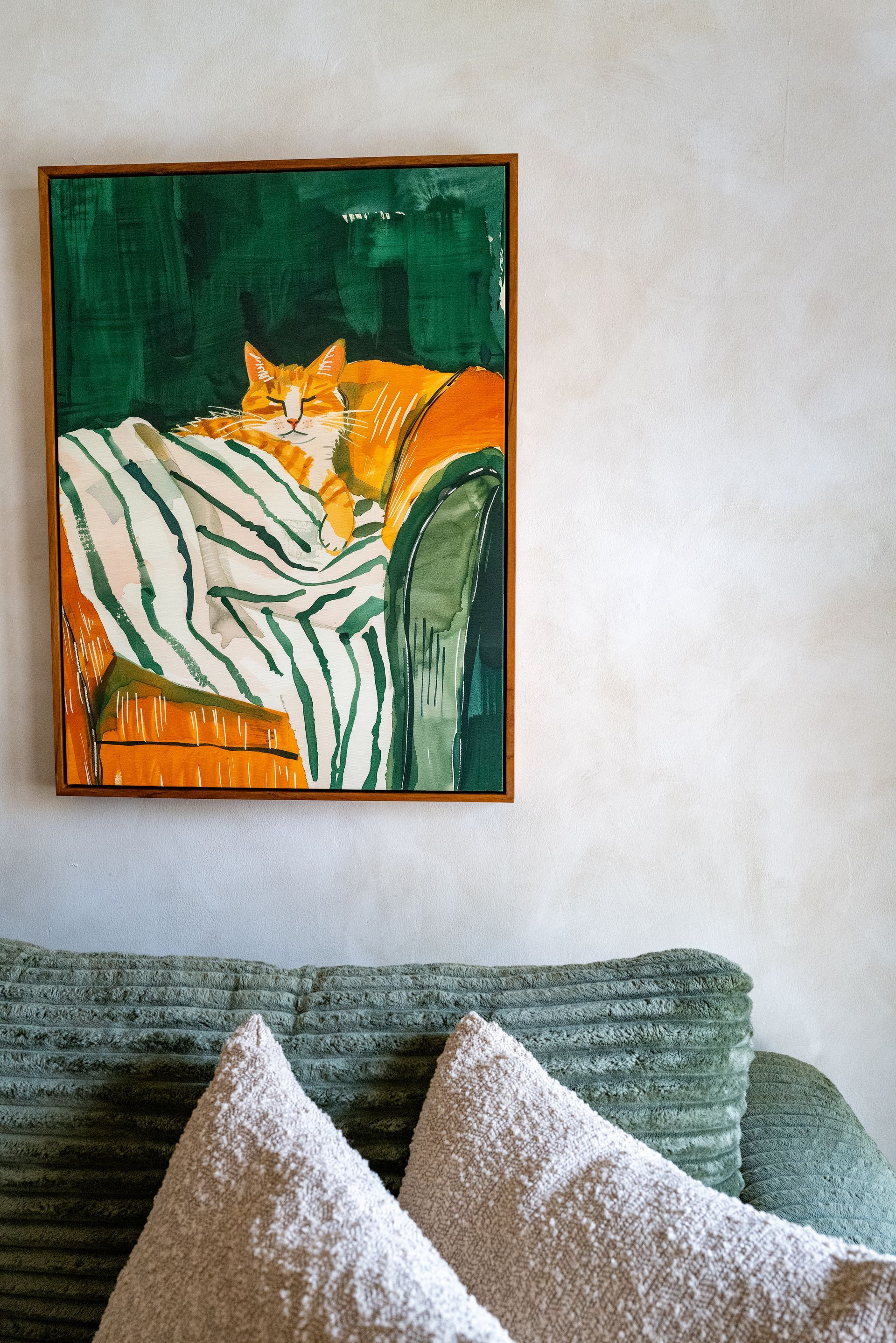 Oil painting of an orange cat resting on a green sofa, framed and mounted on a wall.