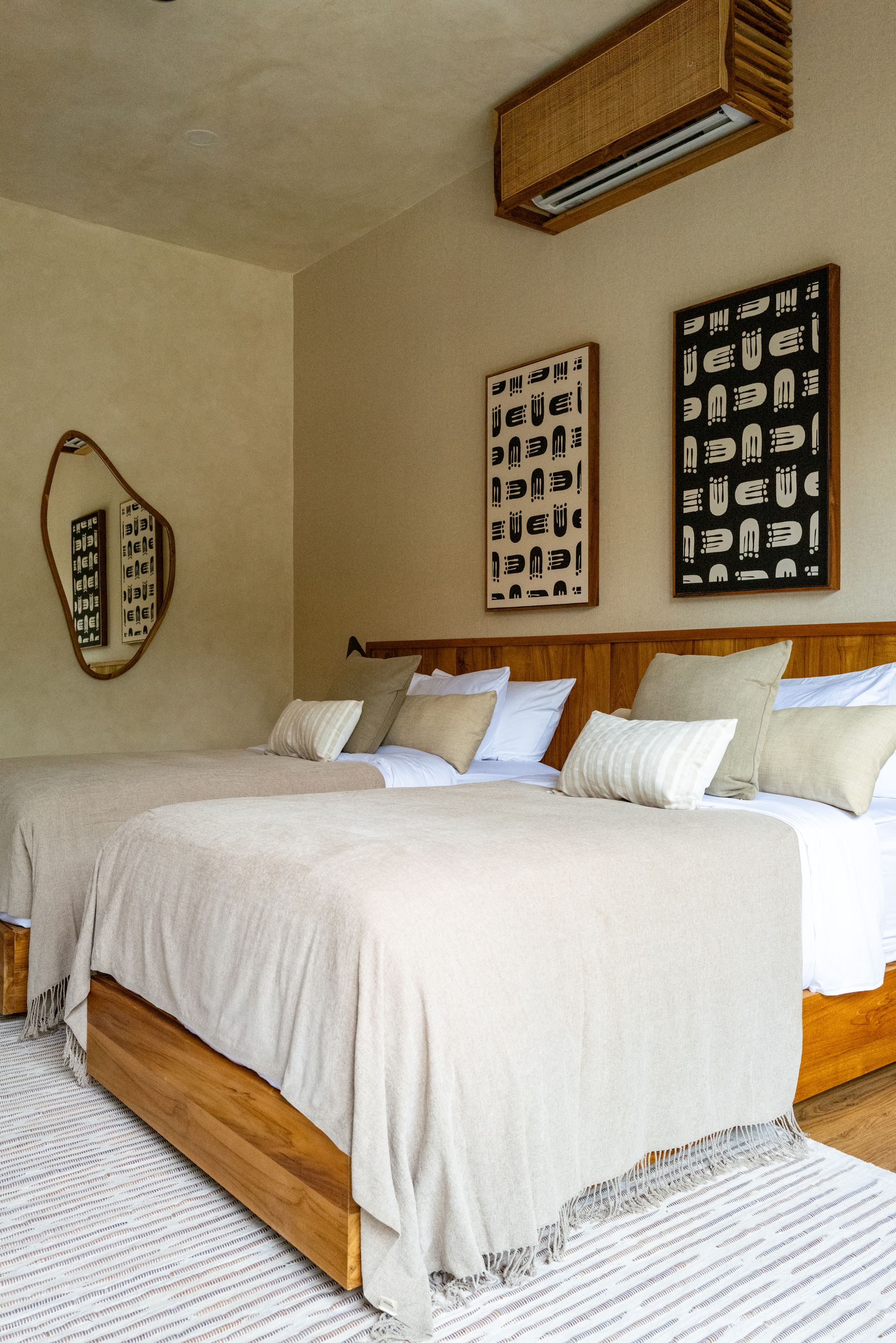 Bedroom with two beds, beige bedding, wooden headboard, art, and patterned rug.