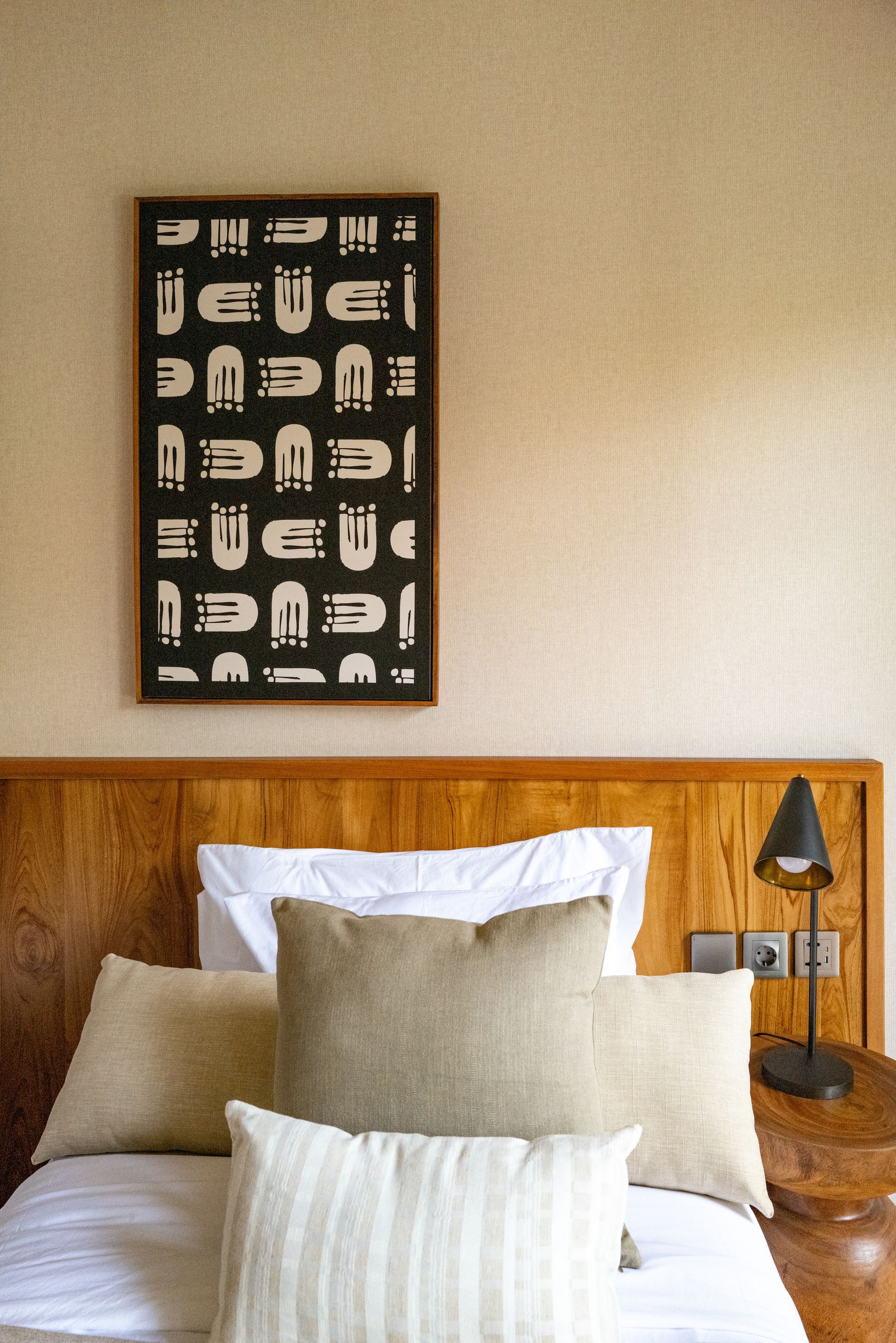 Bedroom scene with a bed, pillows, artwork, and a bedside lamp.