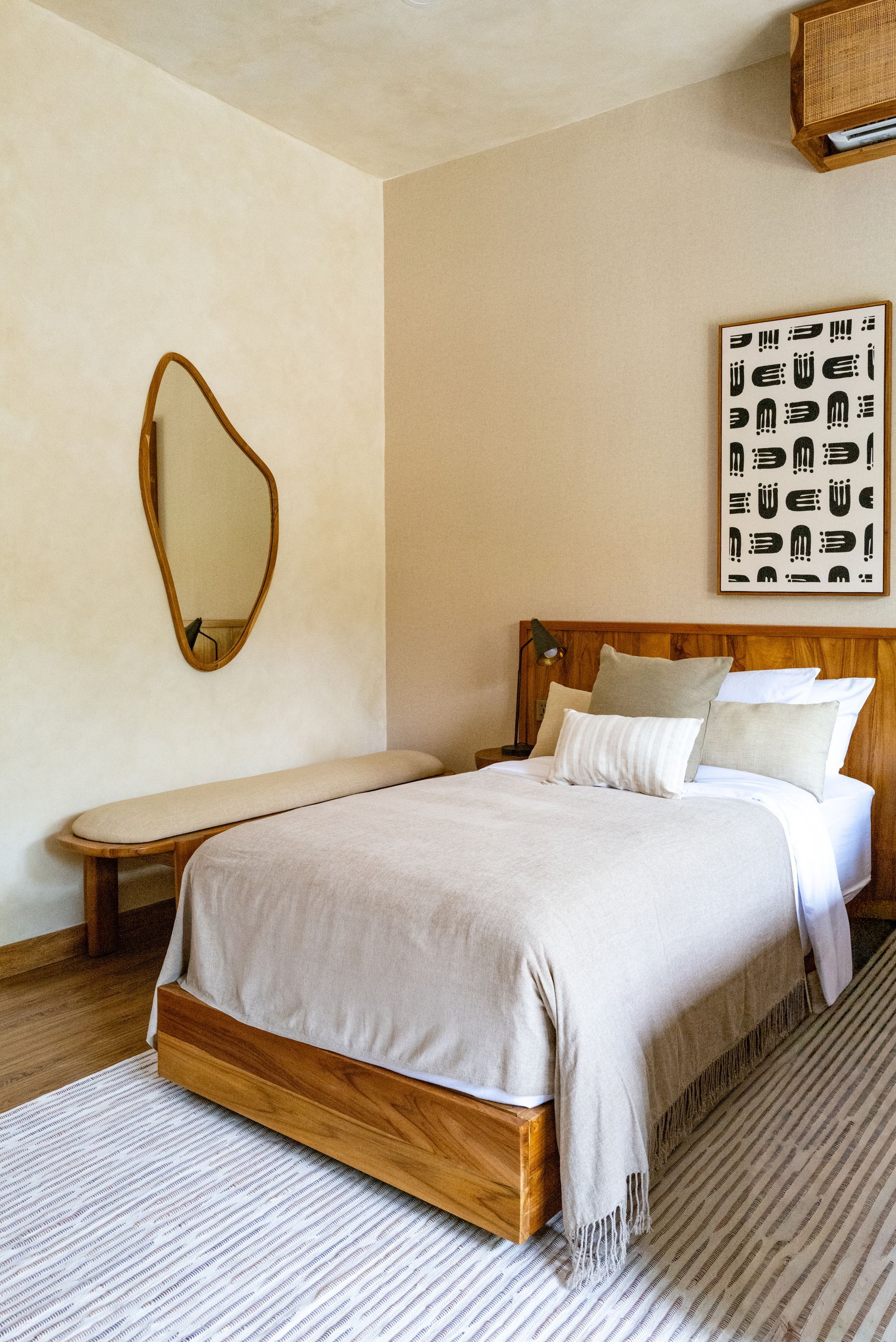 Bedroom with bed, bench, organic mirror, art, and neutral color palette.